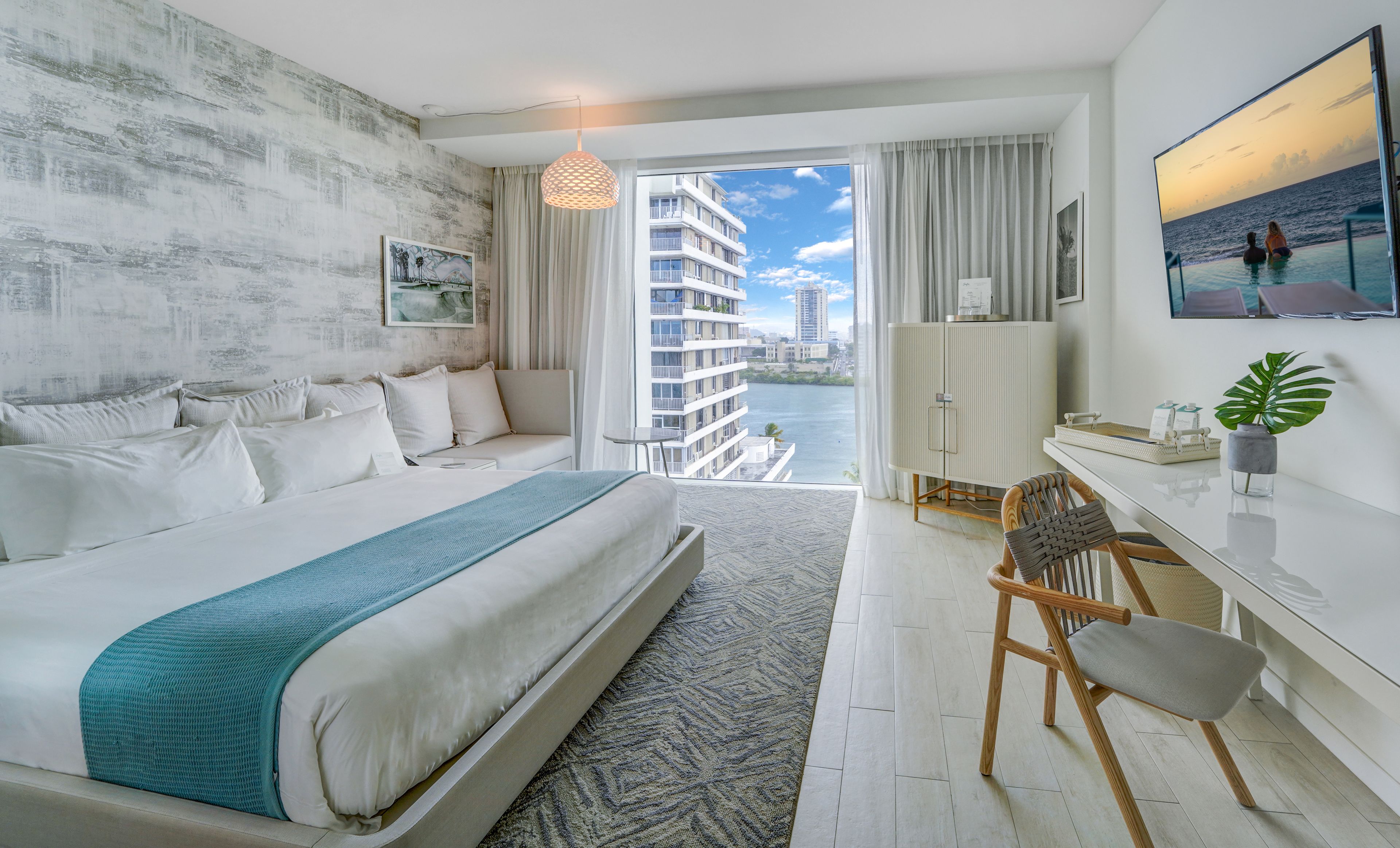 A modern hotel room with a large bed, a desk, and a view of the ocean.