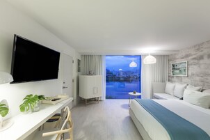Una habitación de hotel moderna con una cama grande, un escritorio con televisión de pantalla plana, una mesita pequeña y vistas a la ciudad a través de un ventanal.