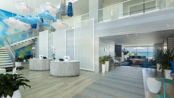 A spacious lobby with a staircase, round tables, potted plants, and hanging blue and white lamps.