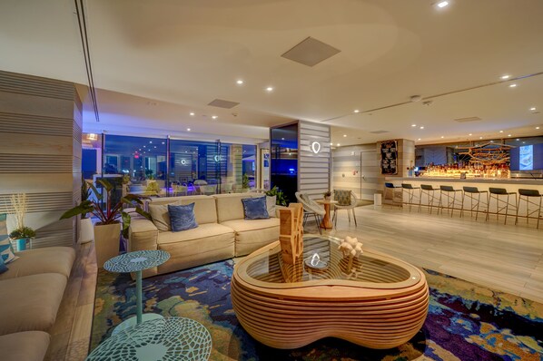 A modern hotel lobby with a sofa, a round wooden coffee table, and a bar area with stools. - Condado Ocean Club - Adults Only (San Juan)