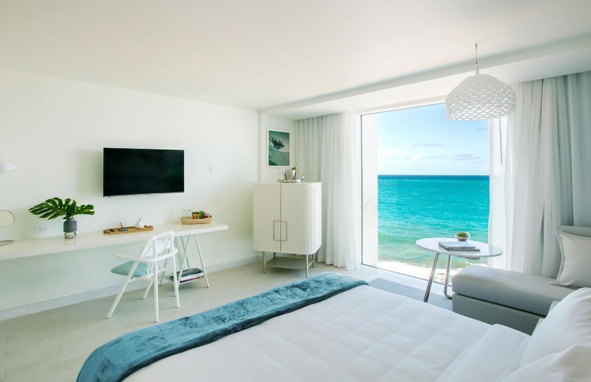 Habitación de hotel moderna con una cama grande, un escritorio, una silla, un televisor y vista al océano.