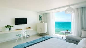 Habitación de hotel moderna con una cama grande, un escritorio, una silla, un televisor y vista al océano.