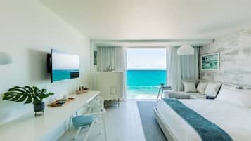 A modern hotel room with a large bed, a desk with a chair, a TV, and a view of the ocean.