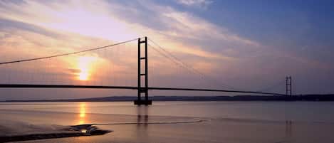 A suspension bridge over a calm body of water during sunset.