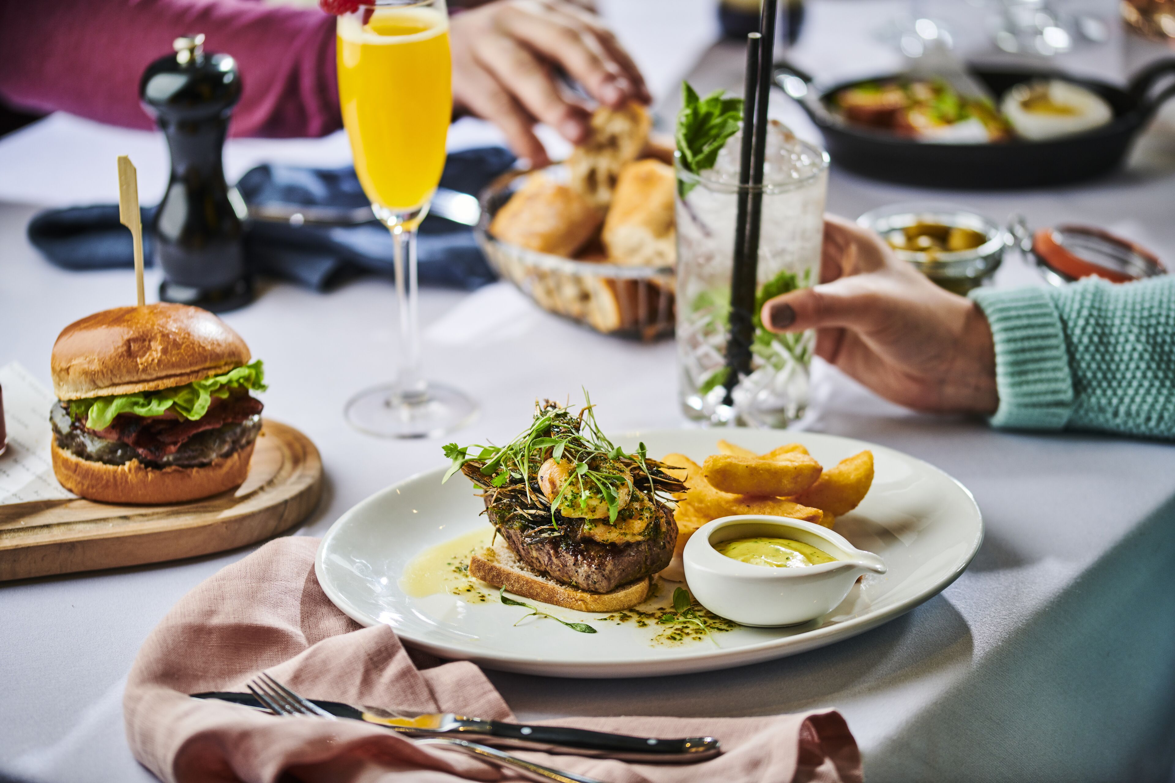 A dining table with a meal consisting of a burger, fries, and a sauce, along with a glass of orange juice.