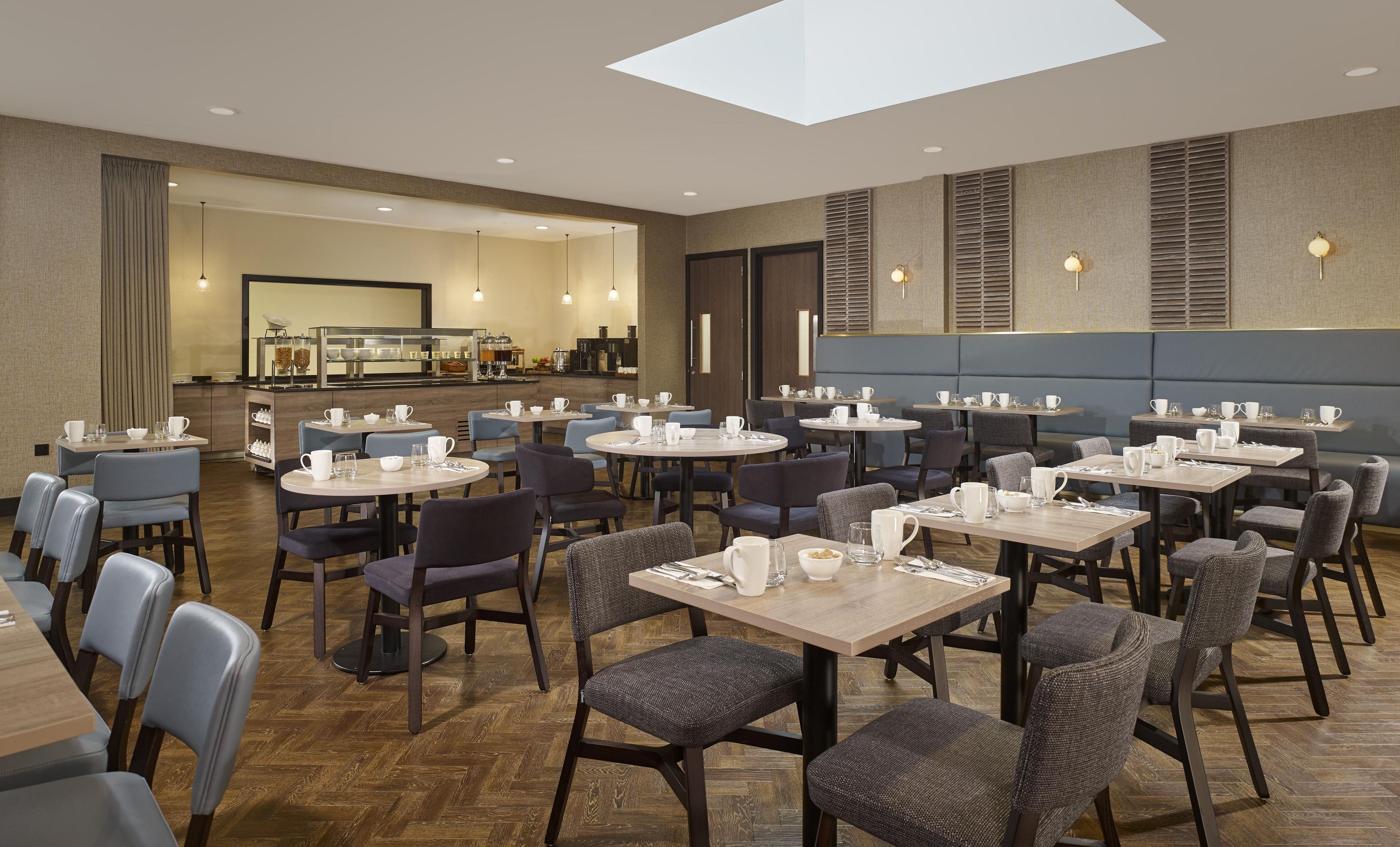 A modern dining area with multiple tables and chairs, a coffee bar, and a skylight.