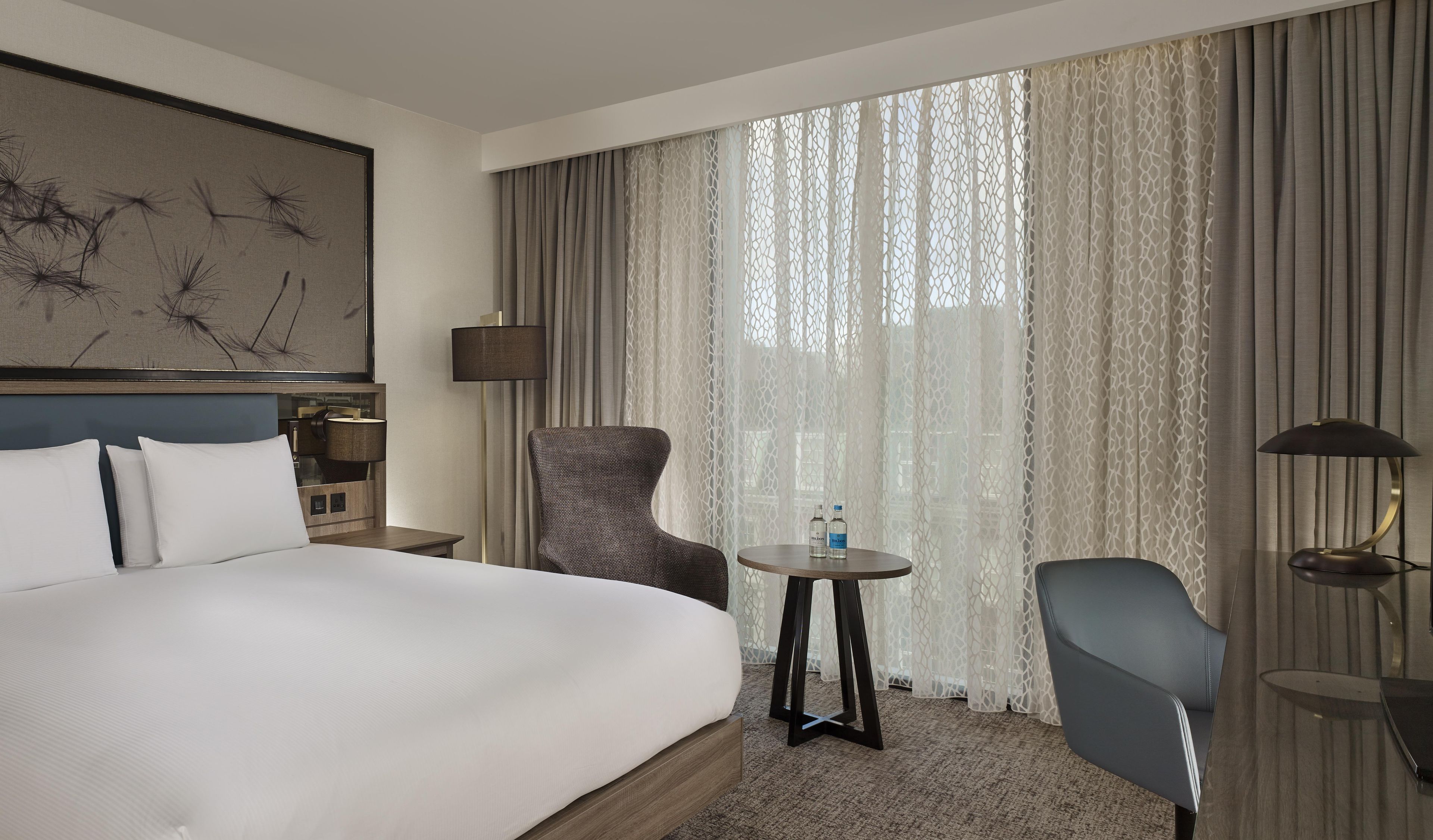 A hotel room with a large bed, a chair, a small table, and a lamp.