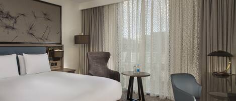 A hotel room with a large bed, a chair, a small table, and a lamp.