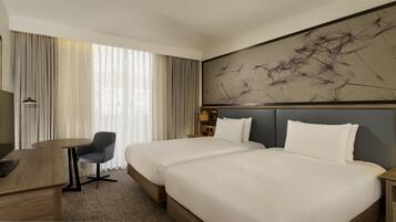 Habitación de hotel con dos camas, un escritorio, una silla y una obra de arte abstracta de gran tamaño en la pared.