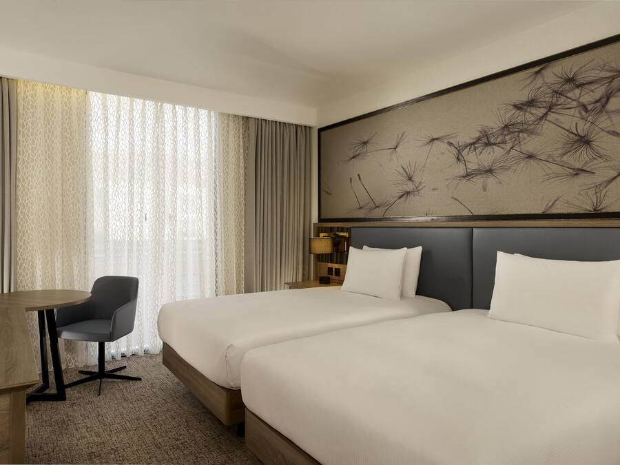 Habitación de hotel con dos camas, un escritorio, una silla y una obra de arte abstracta de gran tamaño en la pared.