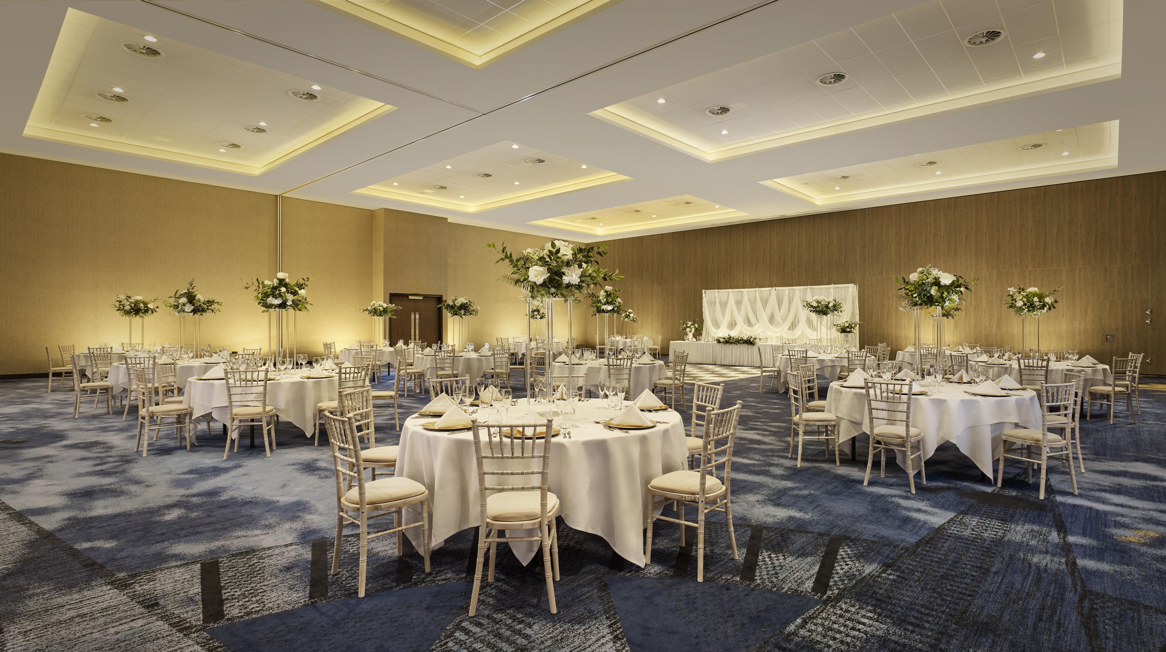 A large banquet hall with round tables, chairs, and floral centerpieces.