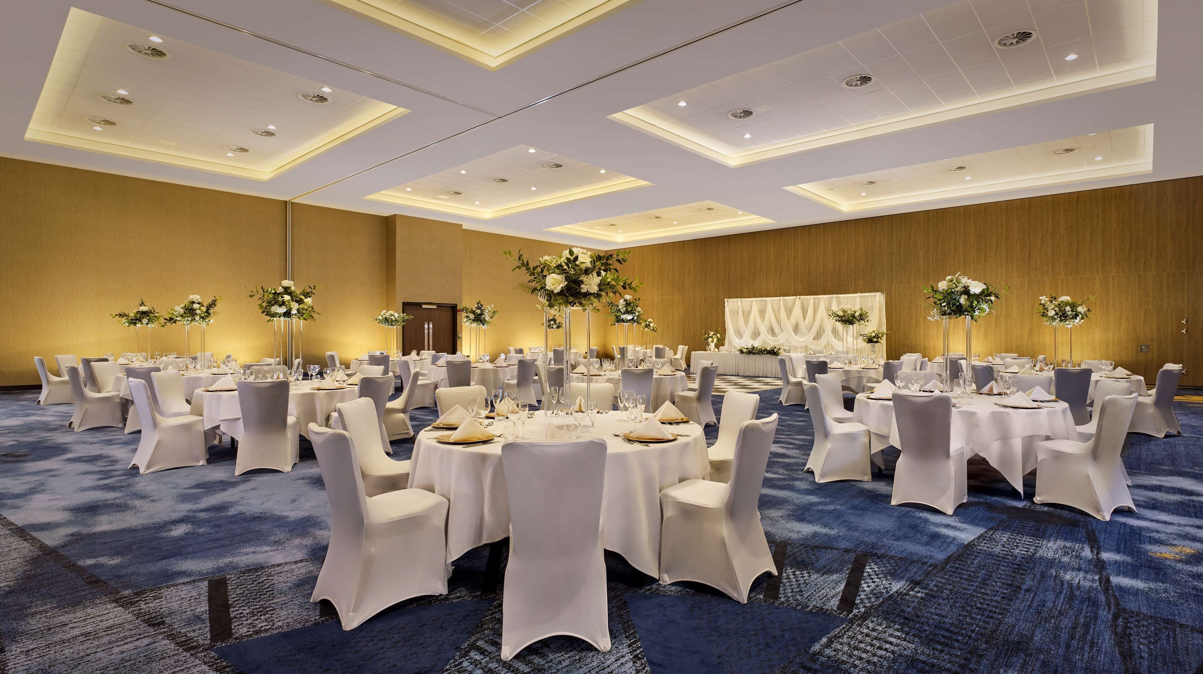 A large banquet hall with round tables, white chairs, and floral centerpieces.