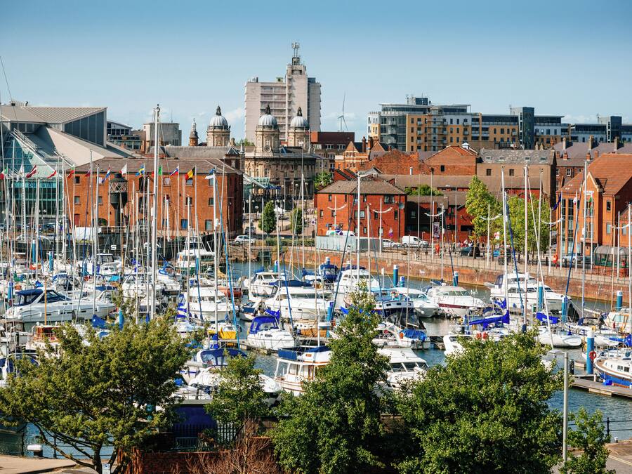 A marina with numerous boats docked, surrounded by buildings with red brick facades and modern architecture.