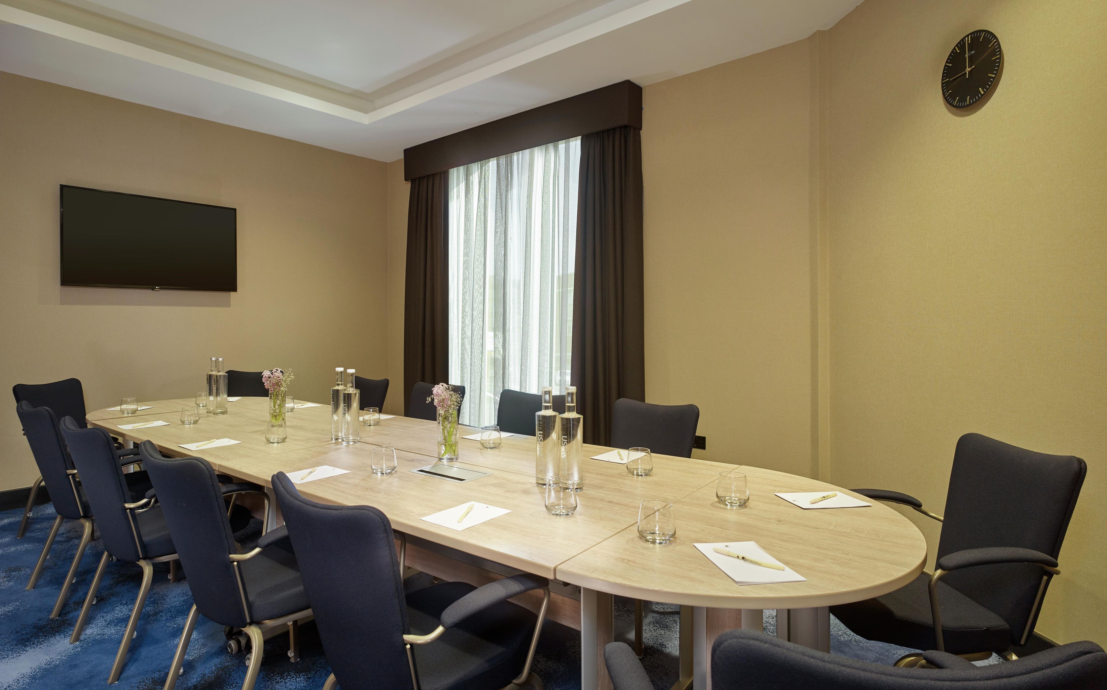 A conference room with a long table, chairs, a clock, and a TV on the wall.