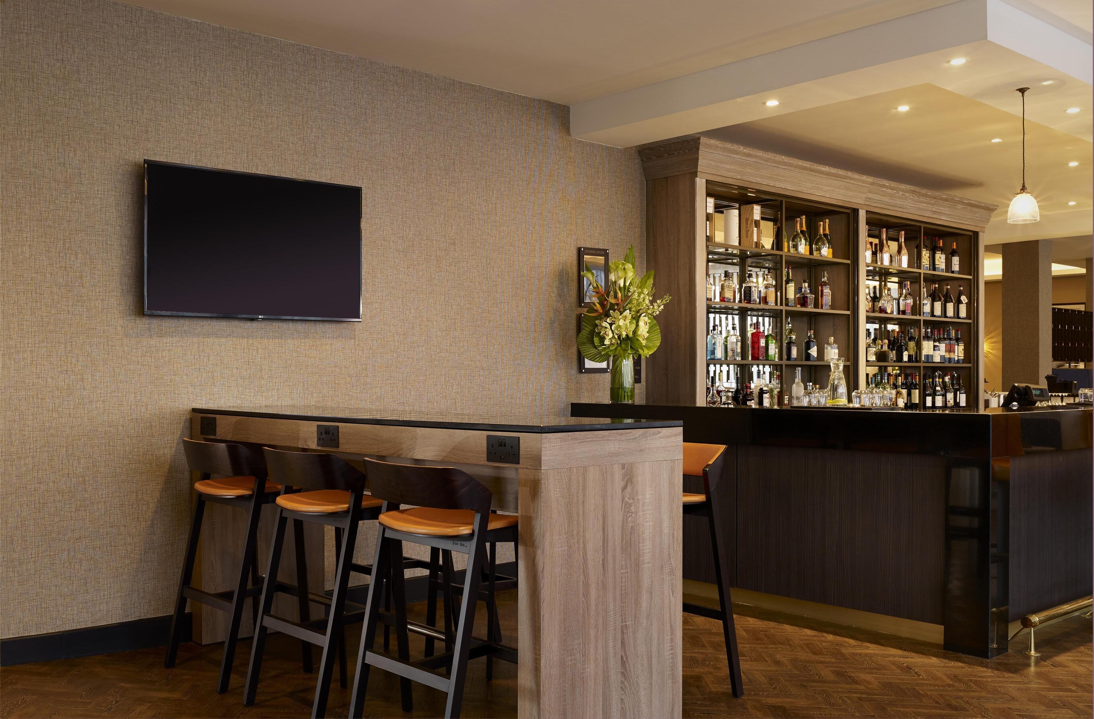 A bar area with a flat-screen TV, bar stools, a wooden counter, and a well-stocked liquor shelf.