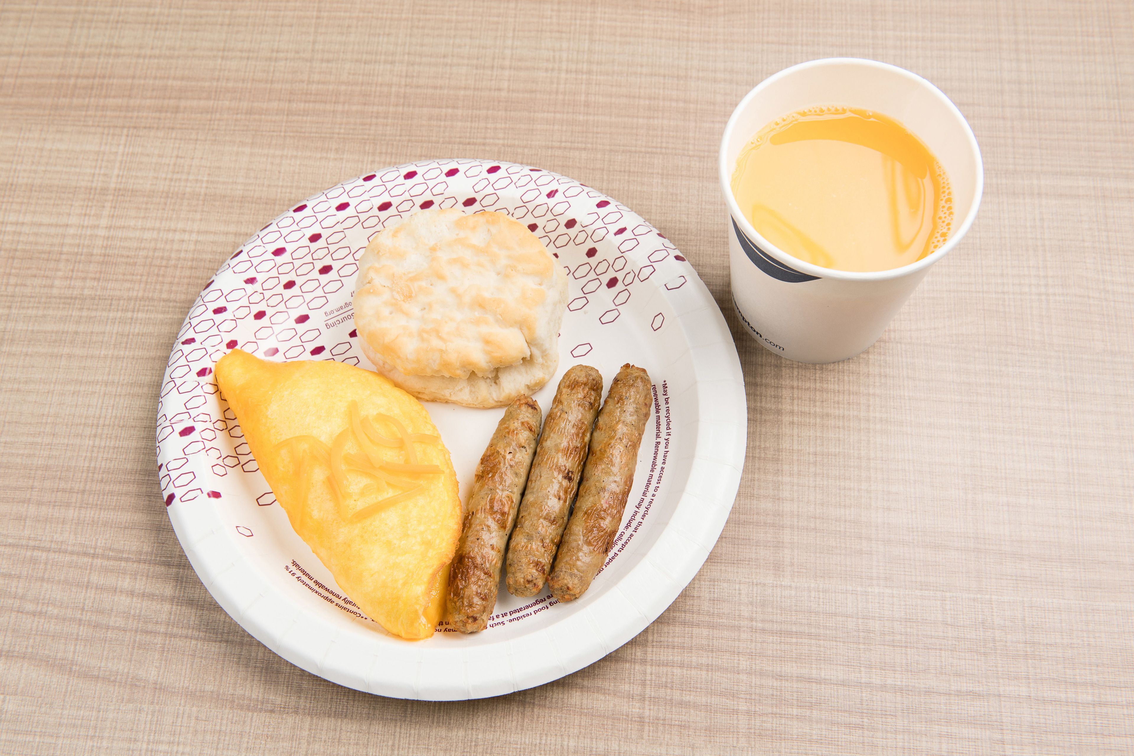 A plate with a biscuit, a slice of orange, and sausages, accompanied by a cup of coffee on a table.