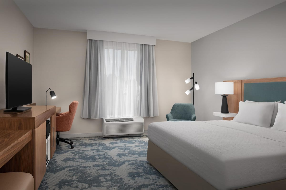 Une chambre d’hôtel équipée d’un lit, d’un bureau, d’une chaise, d’un climatiseur et d’une fenêtre avec des rideaux.