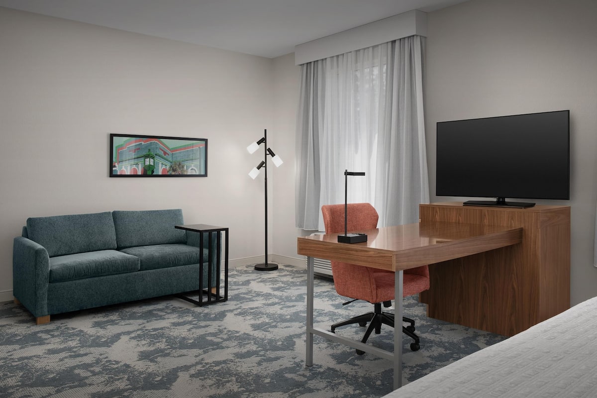 Une chambre d’hôtel équipée d’un canapé, d’un bureau, d’une chaise, d’une télévision et d’œuvres d’art.
