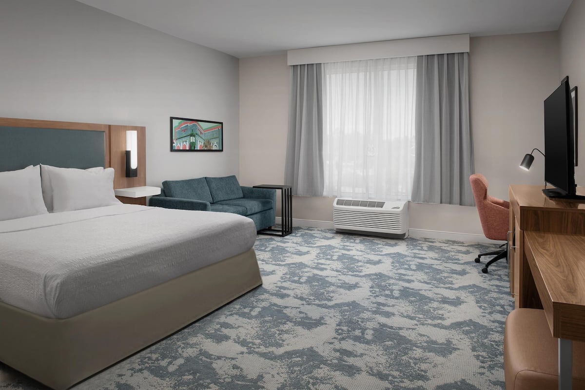 Une chambre d’hôtel avec un grand lit, un bureau avec un ordinateur, une chaise, une télévision et une fenêtre avec des rideaux.
