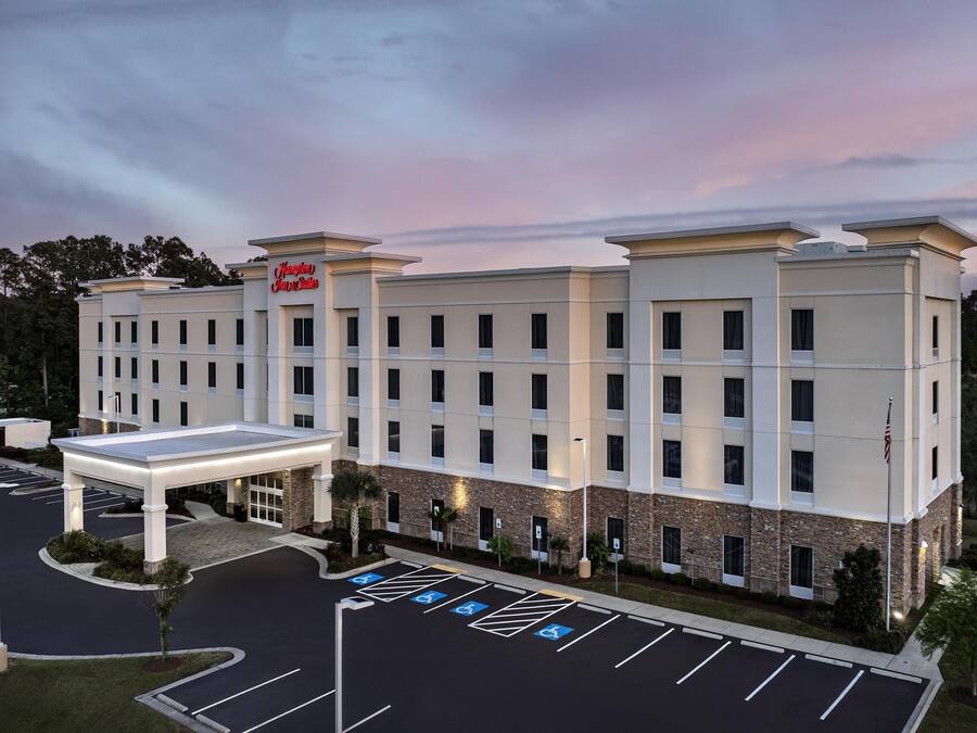 A hotel with a modern design, featuring a large parking lot with handicap-accessible spaces, a covered entrance, and a prominent hotel sign.