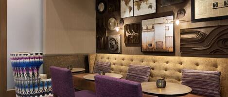 A restaurant with a tufted booth seating area, round tables, and a patterned chair.