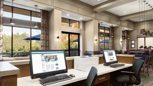 A hotel reception area with two computer workstations, large windows, and a view of the outdoors. - Hampton Inn & Suites Seattle/Renton (Renton)