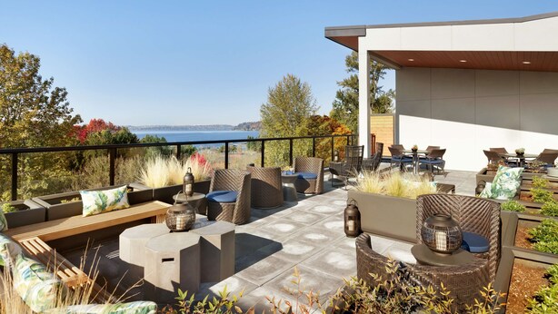 An outdoor patio with seating, a view of the sea, and a modern building structure. - Hampton Inn & Suites Seattle/Renton (Renton)