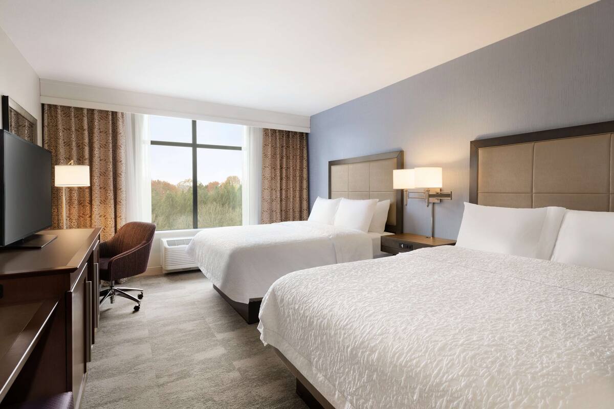 A hotel room with two beds, a desk with a television, and a chair.