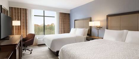 A hotel room with two beds, a desk with a television, and a chair.