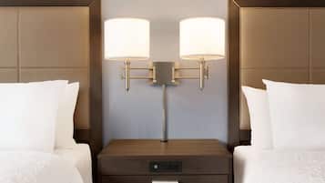 A hotel room with two beds, a nightstand with a digital clock, and wall-mounted lamps.