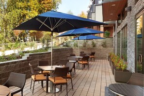 An outdoor patio with tables and chairs, blue umbrellas, and a stone wall.