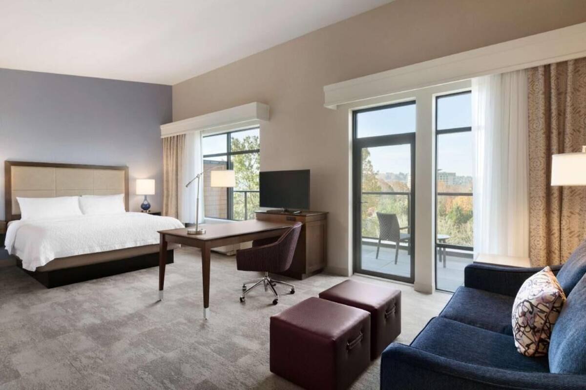 A hotel room with a bed, desk, TV, and a sofa.