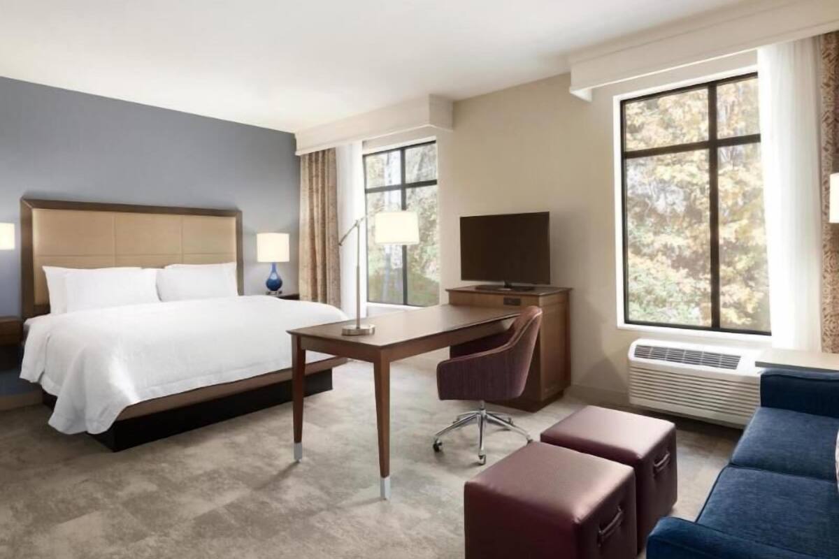 A hotel room with a bed, desk, chair, and a large window.