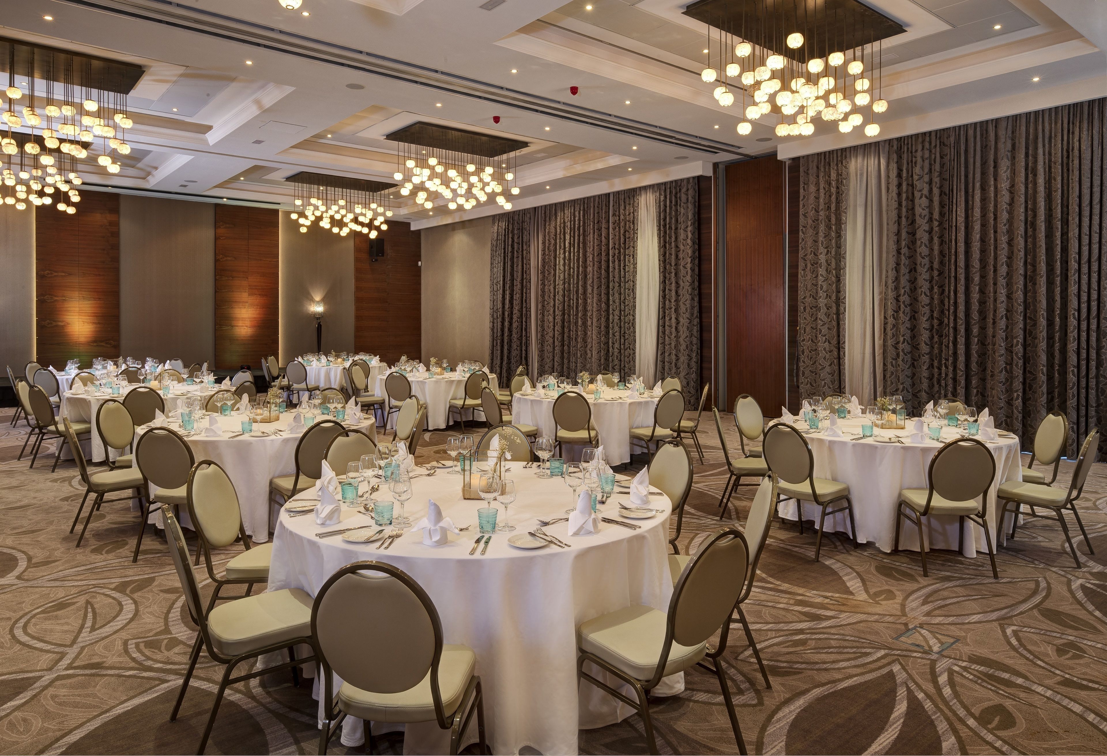 Un salón de banquetes con mesas redondas dispuestas para cenar, con manteles blancos y sillas doradas.