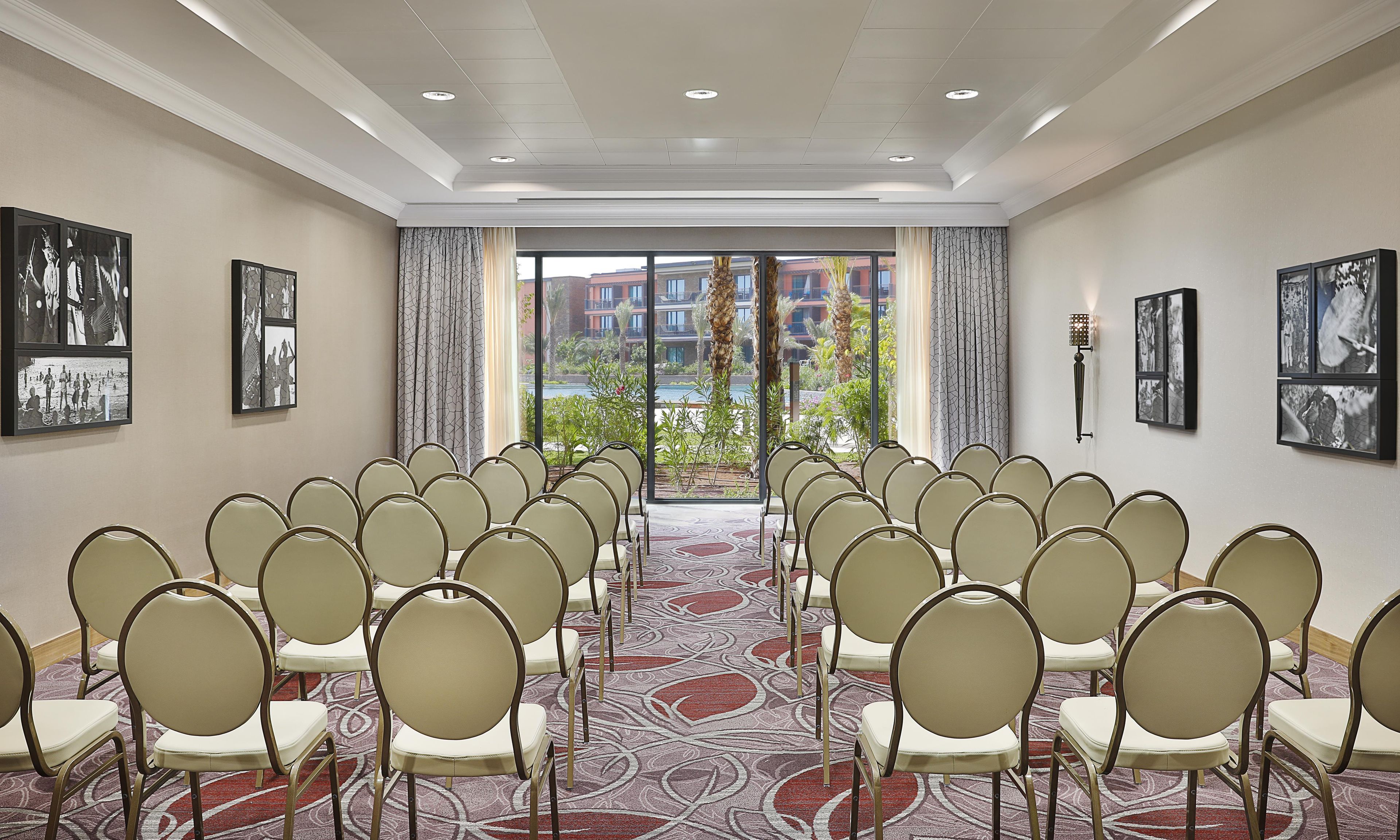 A conference room with rows of chairs facing a large window with a view of buildings and a pool.