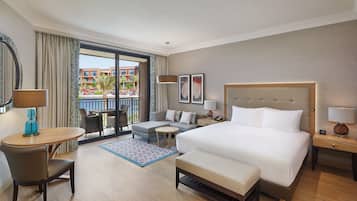 A hotel room with a large bed, a desk, a chair, a sofa, and a balcony with a pool view.