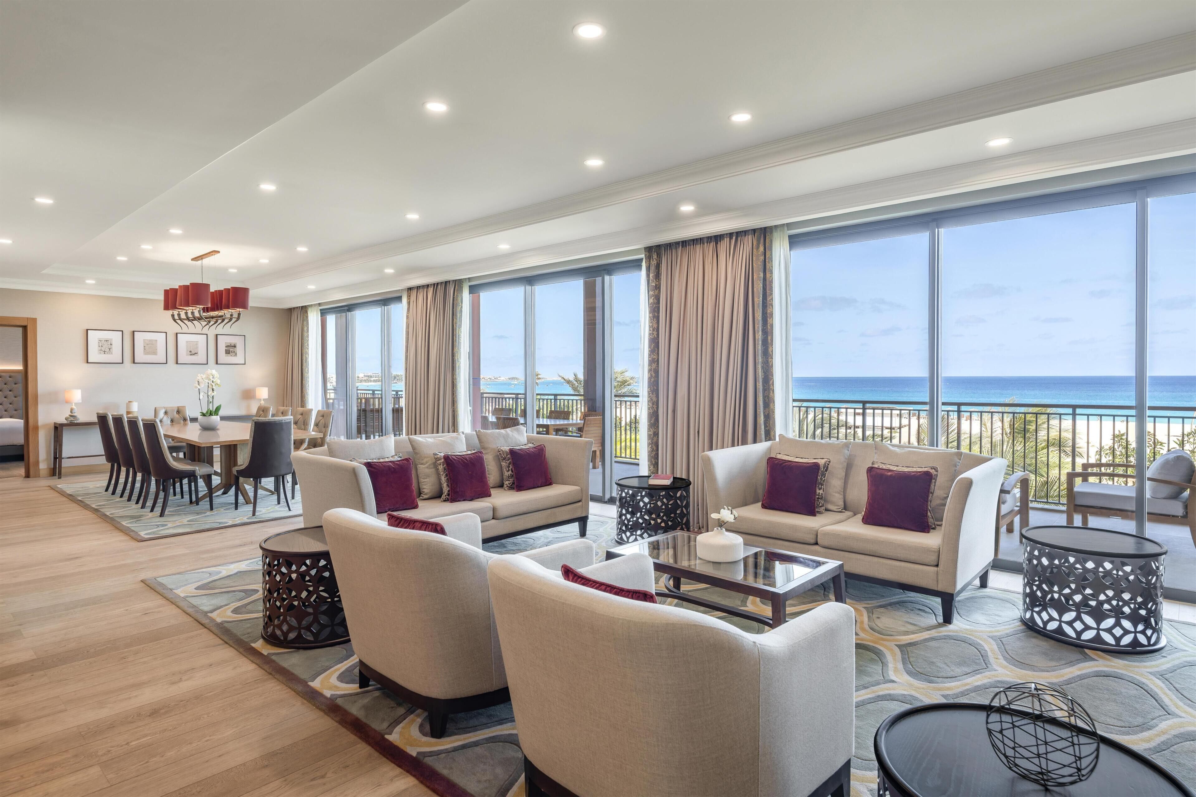 A spacious living area with a large window overlooking the sea, a dining area, and a seating arrangement with sofas and a coffee table.