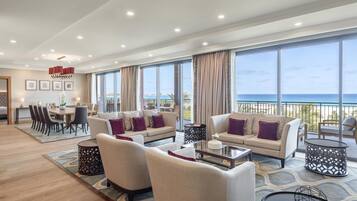 A spacious living area with a large window overlooking the sea, a dining area, and a seating arrangement with sofas and a coffee table.