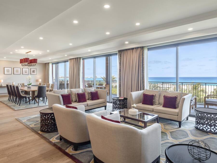 A spacious living area with a large window overlooking the sea, a dining area, and a seating arrangement with sofas and a coffee table.