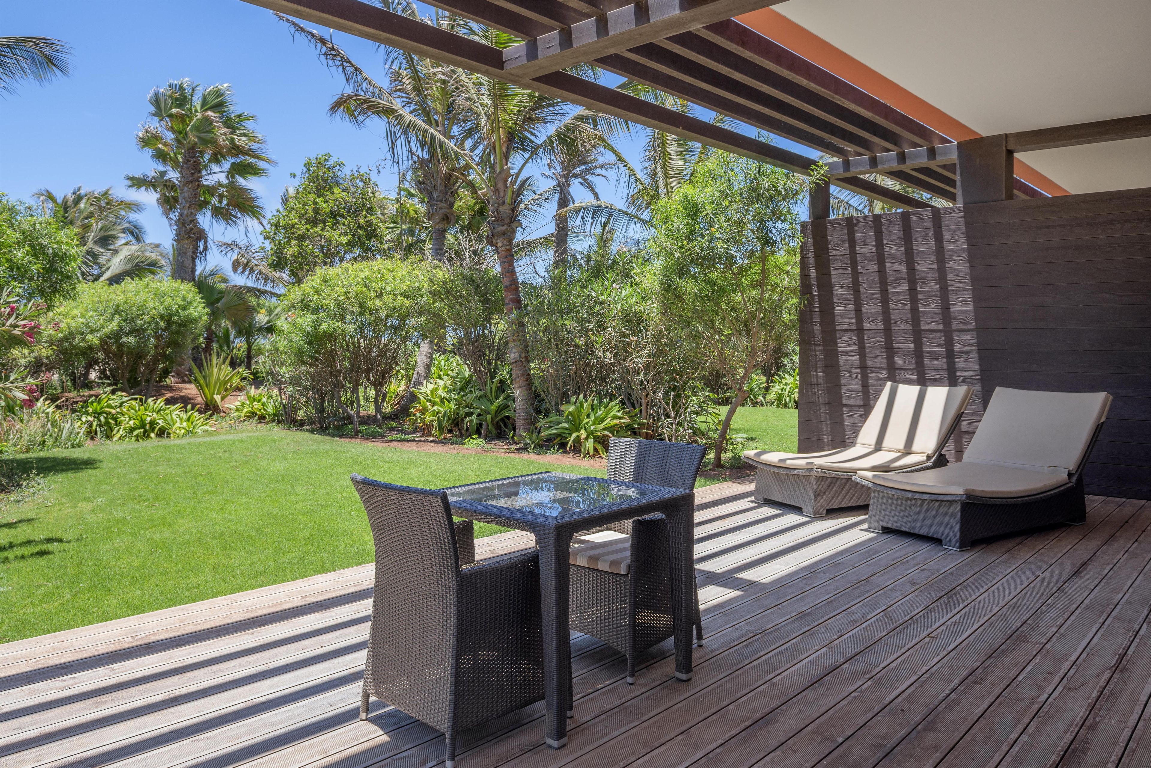 A deck with wicker furniture, a glass-top table, and lounge chairs.