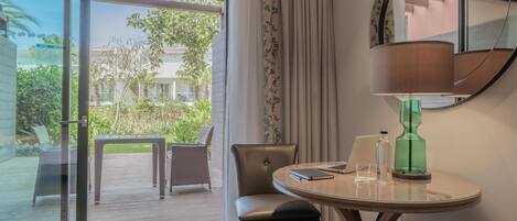 Une chambre d’hôtel avec une porte vitrée donnant sur une terrasse extérieure, une table ronde avec une lampe, une chaise et une petite table d’appoint.
