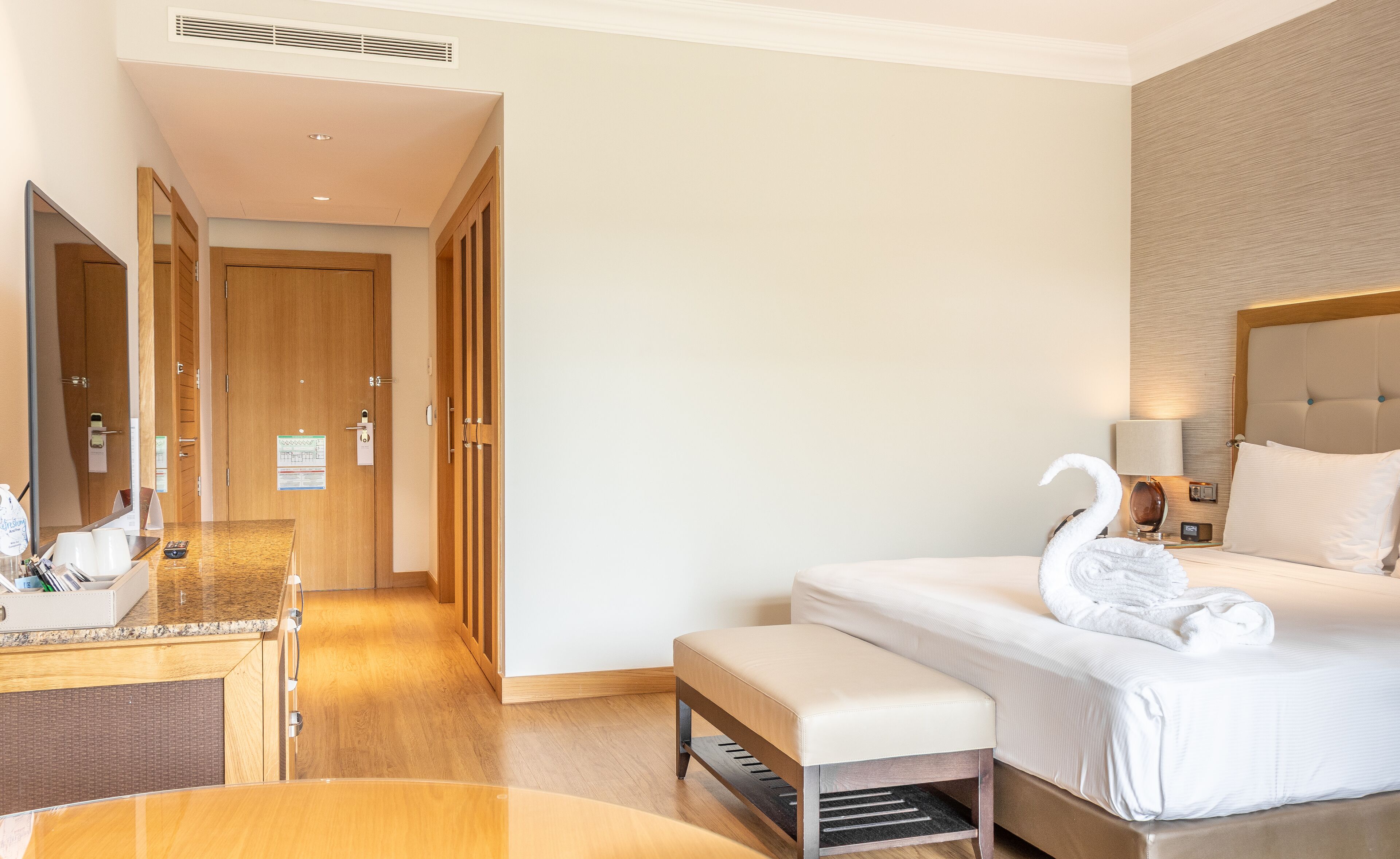 A hotel room with a bed, a bench, a desk with a mirror, and a wardrobe.