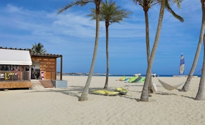 A beach scene with a wooden building, palm trees, and beach equipment.