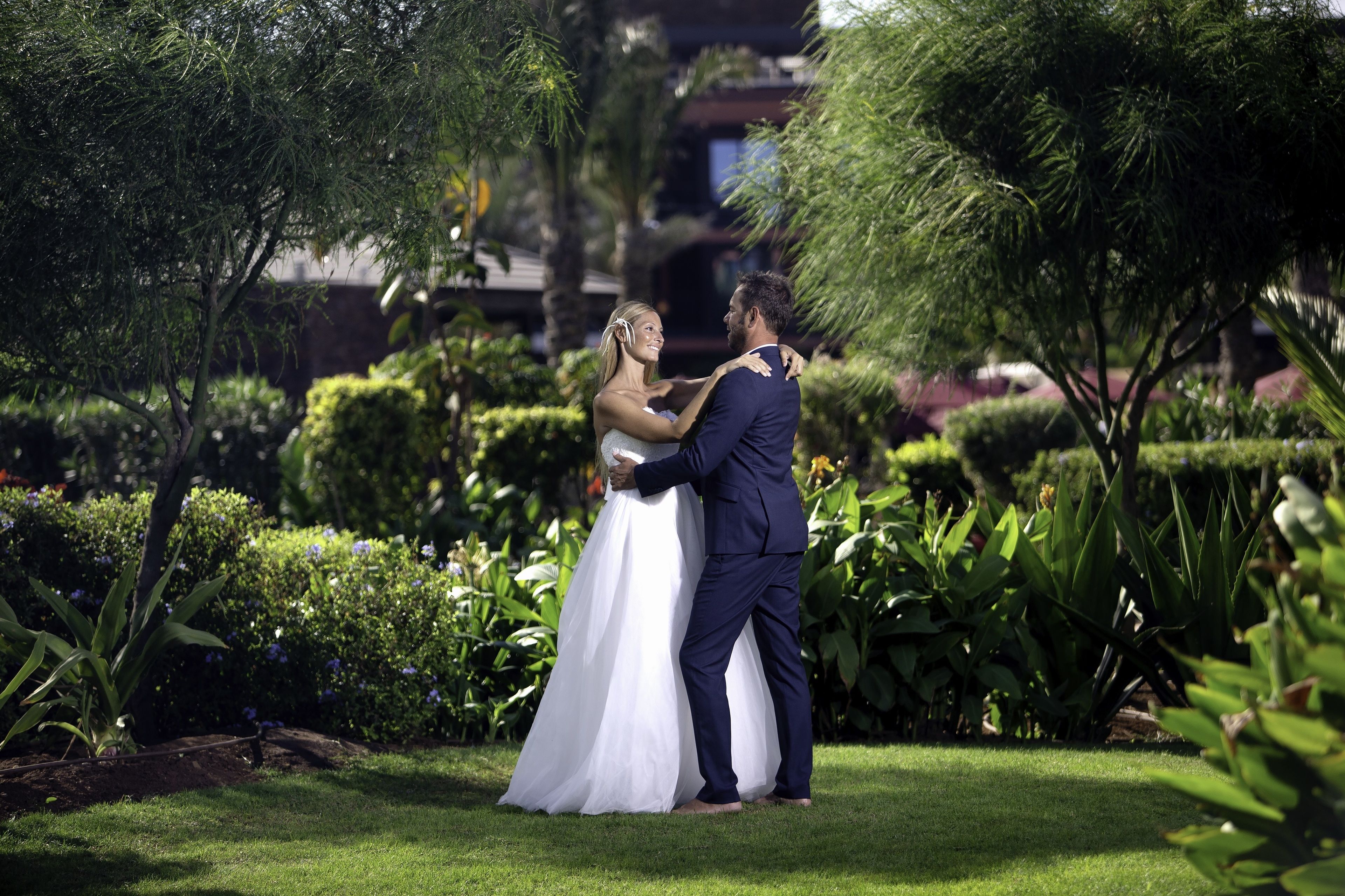 Una pareja abrazándose en un jardín con setos y árboles bien cuidados.