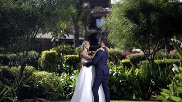 Una pareja abrazándose en un jardín con setos y árboles bien cuidados.