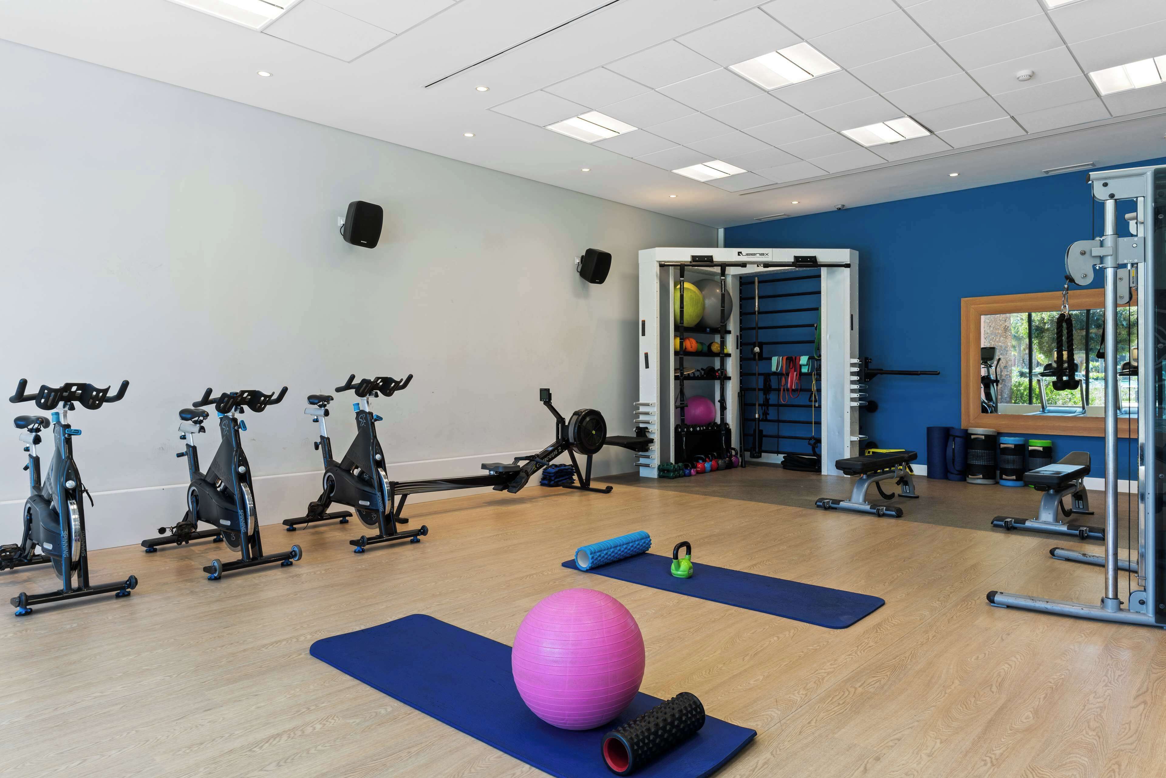 Een sportschool met hometrainers, een grote roze fitnessbal en diverse fitnessapparaten.