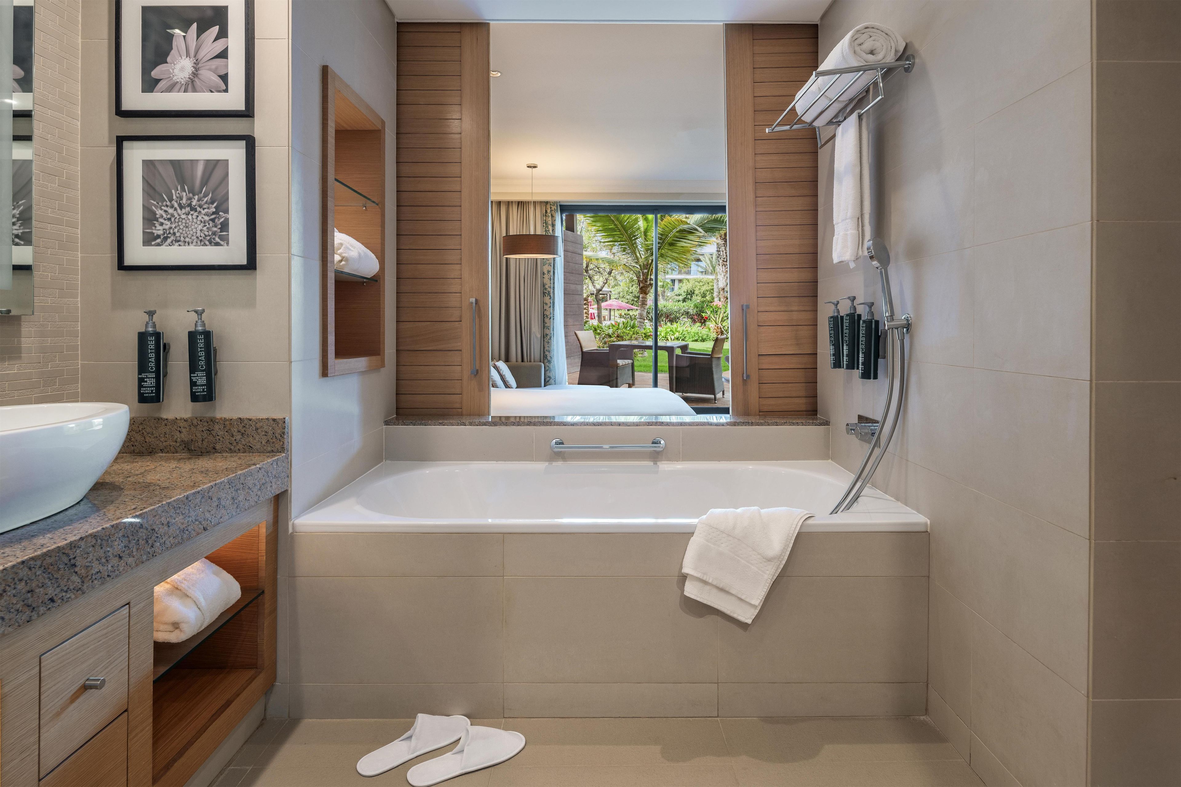 Une salle de bain moderne avec une baignoire, un grand miroir et une vue sur un espace extérieur.