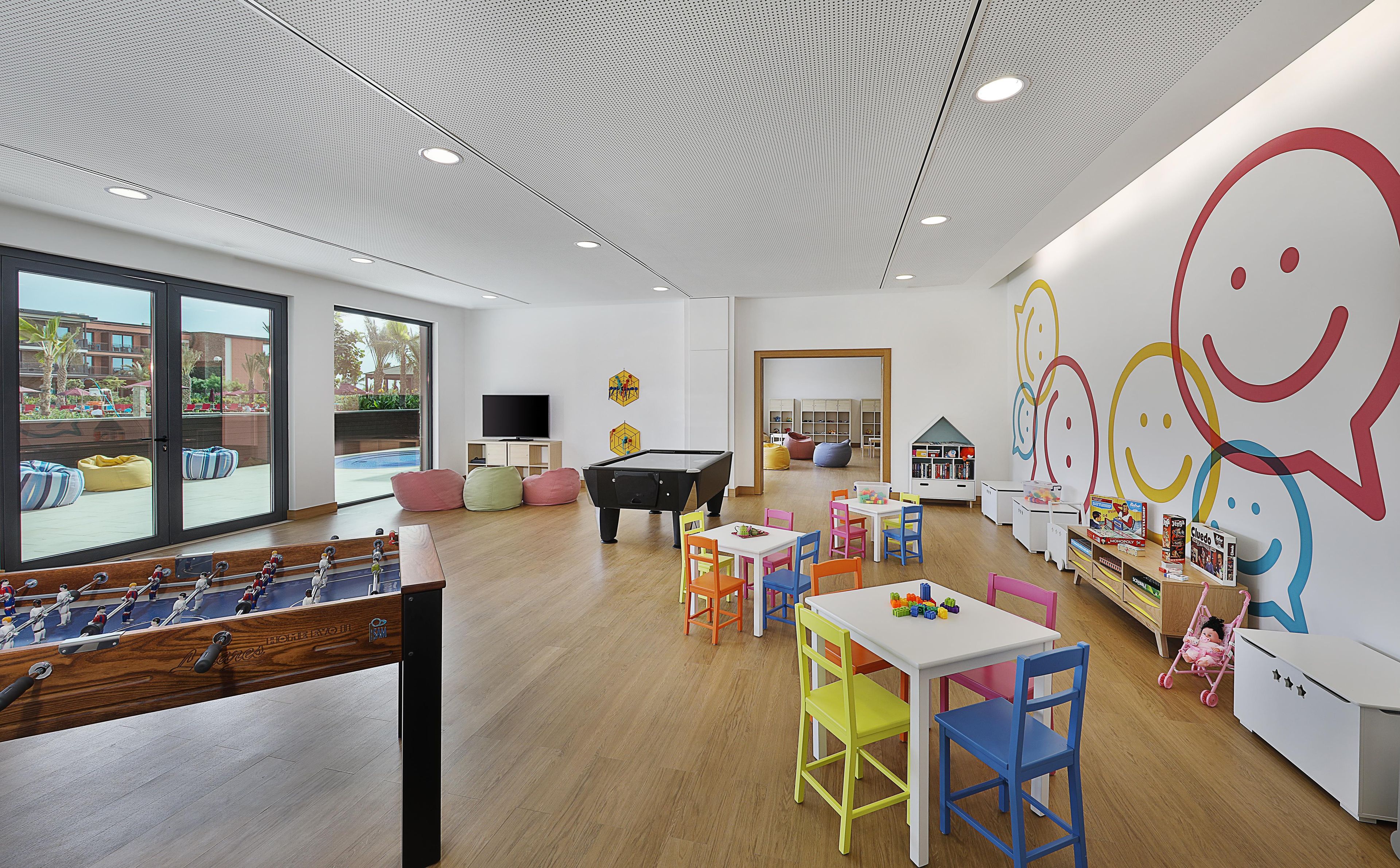 A children's play area with a pool table, colorful chairs, and a large wall mural.