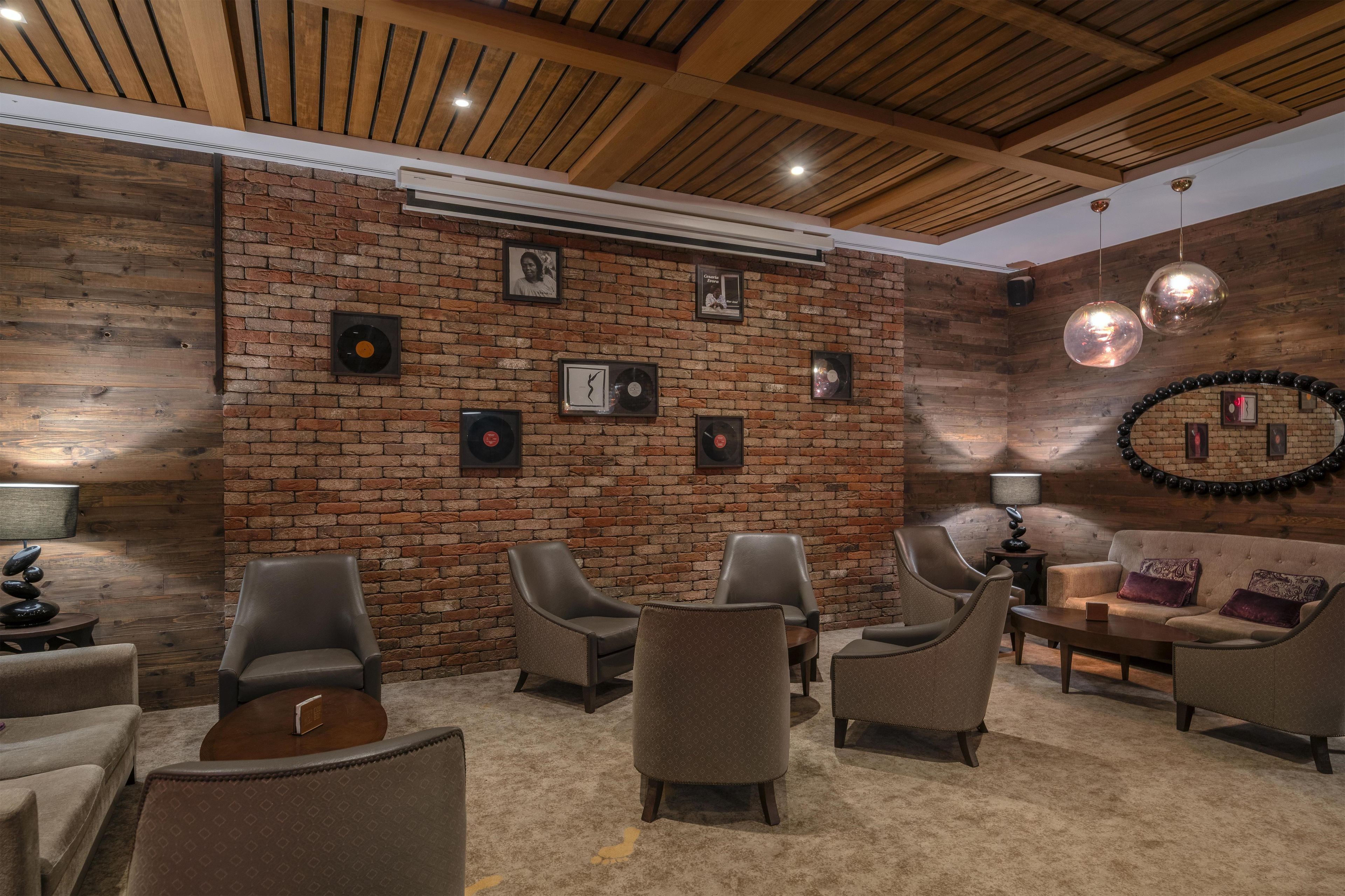 A cozy lounge area with a brick wall, multiple seating options, and a ceiling with wooden beams.