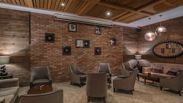 A cozy lounge area with a brick wall, multiple seating options, and a ceiling with wooden beams.